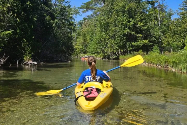 a man riding on the back of a boat next to a lake
