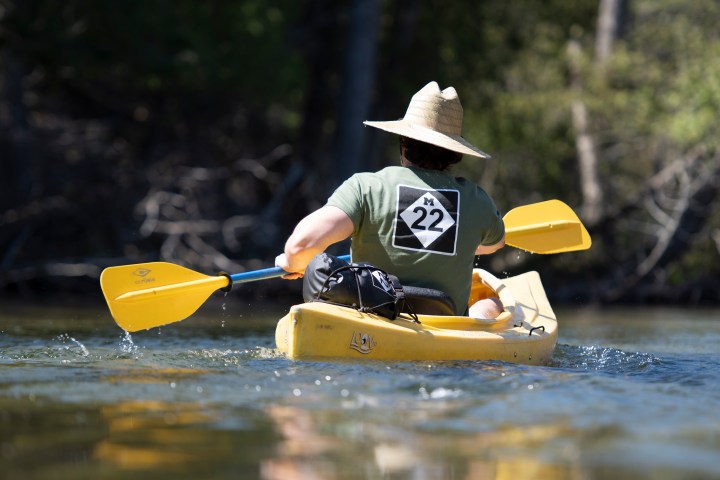 Person in yellow kayak on lake, wearing straw hat and green shirt with 'M 22' design.
