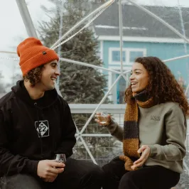A man and woman sitting and laughing together inside a clear geodesic dome.