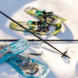 Two pairs of snowshoes and hiking poles on snow.