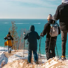 Four people with hiking poles walking on snowy cliffs overlooking the sea.