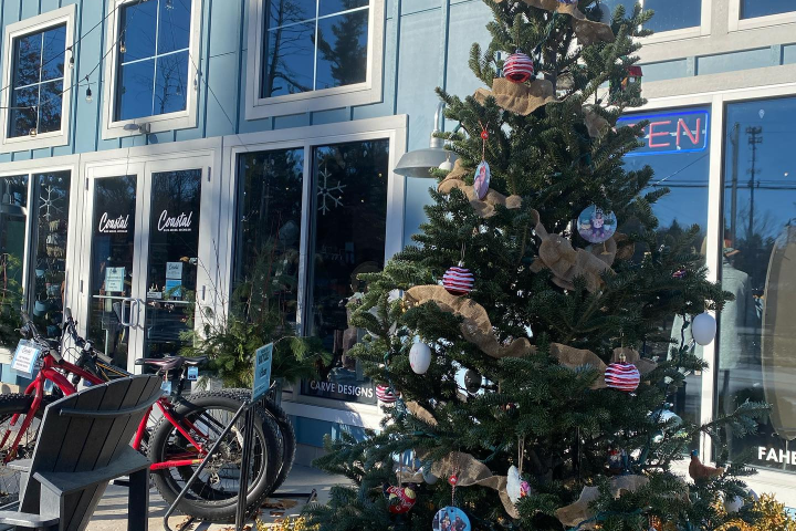 Christmas tree with ornaments outside a clothing store with blue exterior and bikes.
