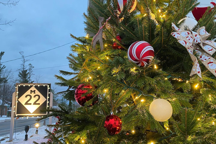 Decorated Christmas tree with lights and ornaments, road sign in snowy urban setting.
