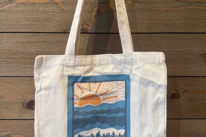 Canvas tote bag with a coastal print design hanging on a wooden wall.