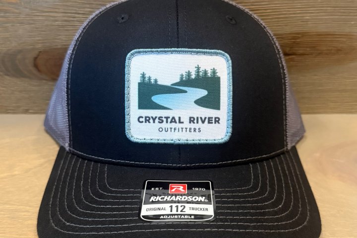 Black and gray cap with 'Crystal River Outfitters' logo on a wooden surface.