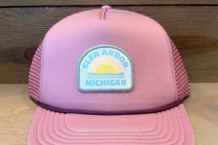 Pink cap with 'Glen Arbor Michigan' patch featuring a sunset design, wooden background.