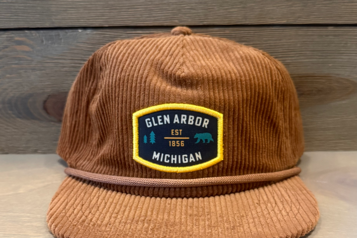 Brown corduroy hat with 'Glen Arbor Michigan' patch on wooden background.