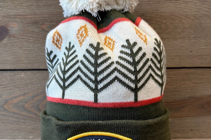 Knit beanie with a pom-pom, tree design, and Glen Arbor Michigan patch on a wooden background.