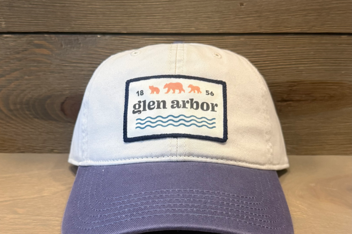 Baseball cap with 'glen arbor' and bear design on patch, light gray top, purple brim, wood background.