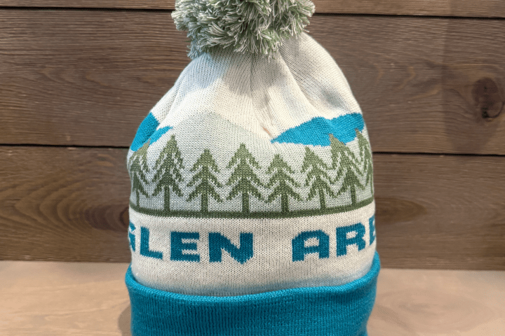 Knit winter hat with mountain and tree design, topped with a pom-pom.
