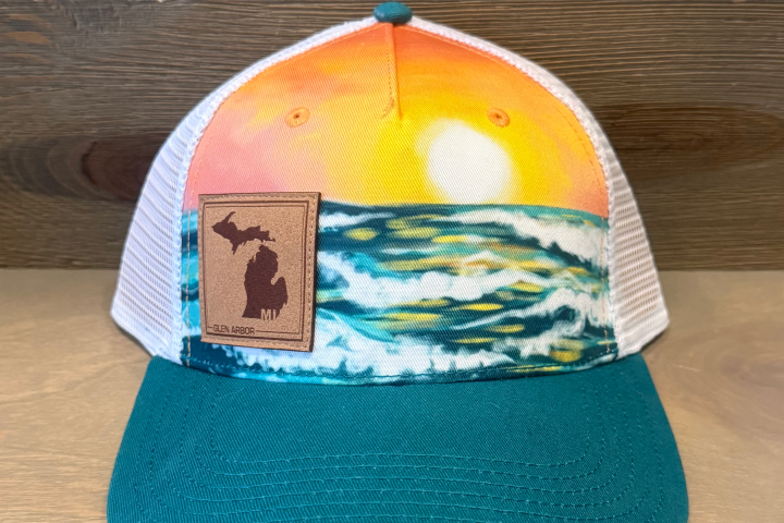 Colorful hat with ocean scene and leather patch of Michigan state on front, wood wall background.