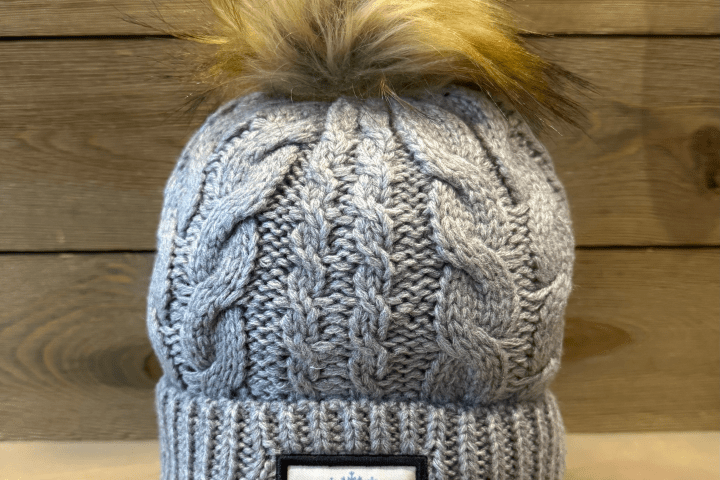 Gray knit beanie with faux fur pom-pom and 'Michigan' patch on wooden background.