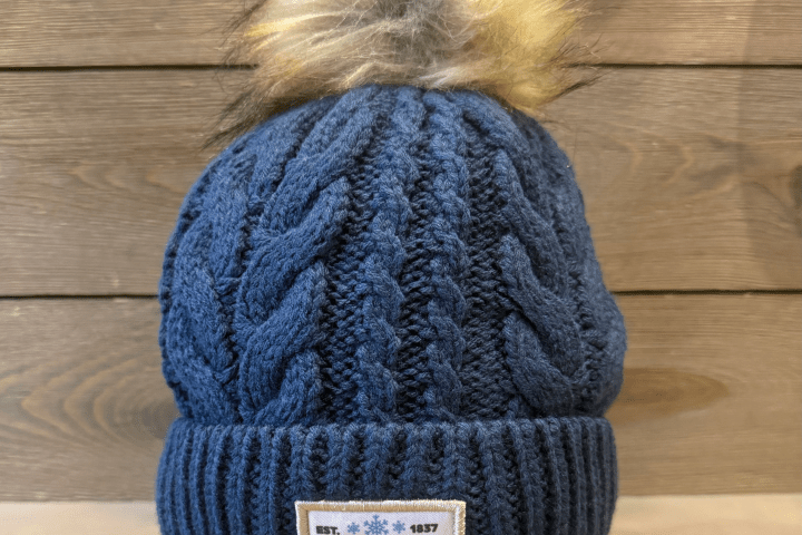Blue knitted beanie with pom-pom and 'Michigan' patch on wood background.