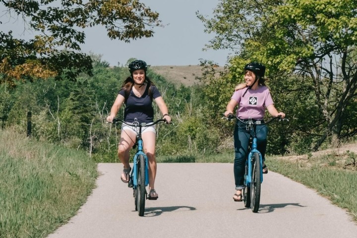 Two people biking on a scenic path with green trees and grass.