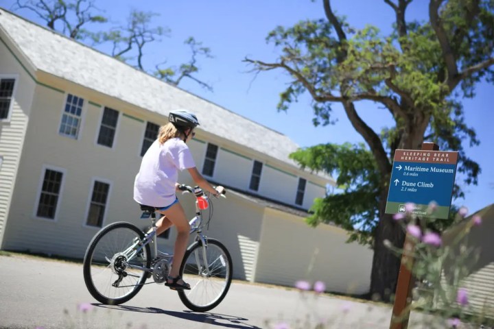 Person cycling near a building with a directional sign and trees.