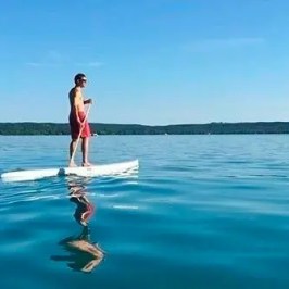 Person paddleboarding on calm blue water with clear sky.